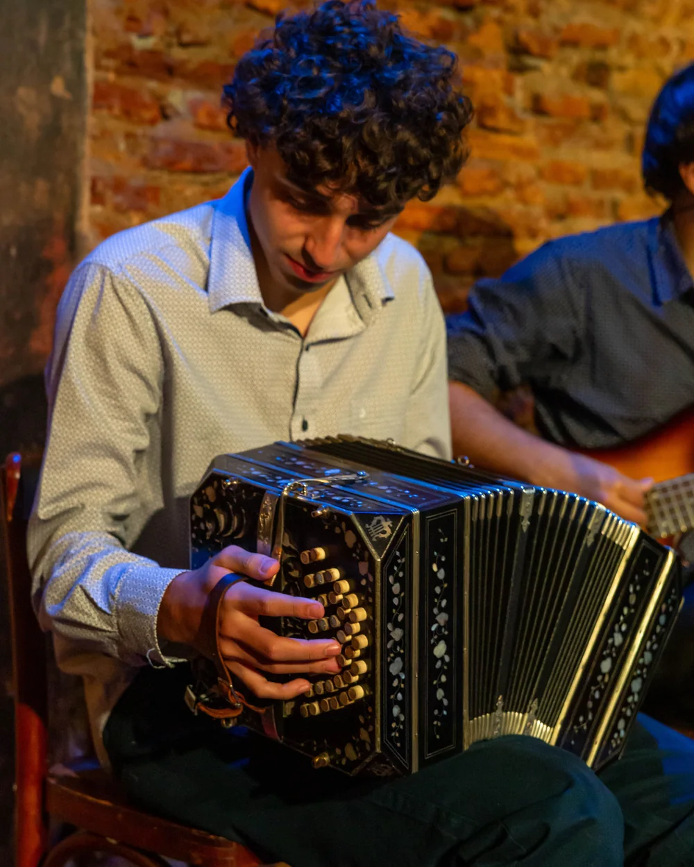 A young musician playing a bandoneón in Argentina, another musician beside him (representative photograph of a Rioplatense tango band, not Primuseum's own trio)